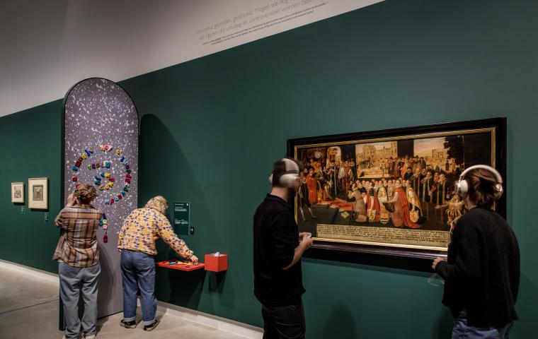 Twee bezoekers met hoofdtelefoon kijken naar een schilderij.