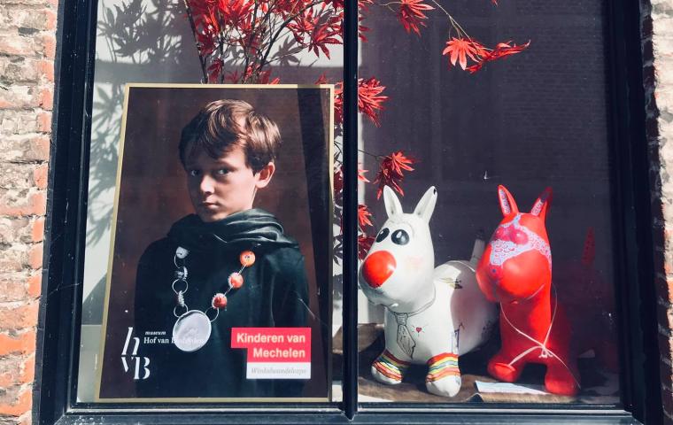 In een raam hangt een poster van een kind met mantel en ketting.