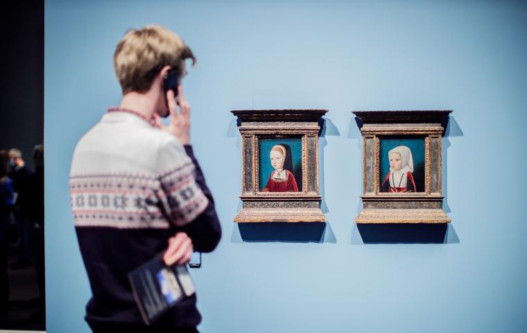 Een bezoeker met audiogids kijkt naar twee kleine portretten.