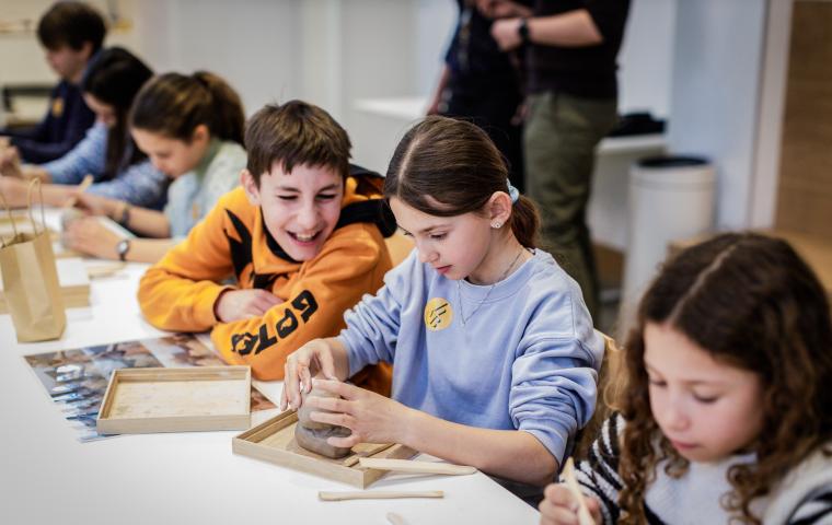 Een groep kinderen zit aan tafel te knutselen, twee kinderen lachen samen.