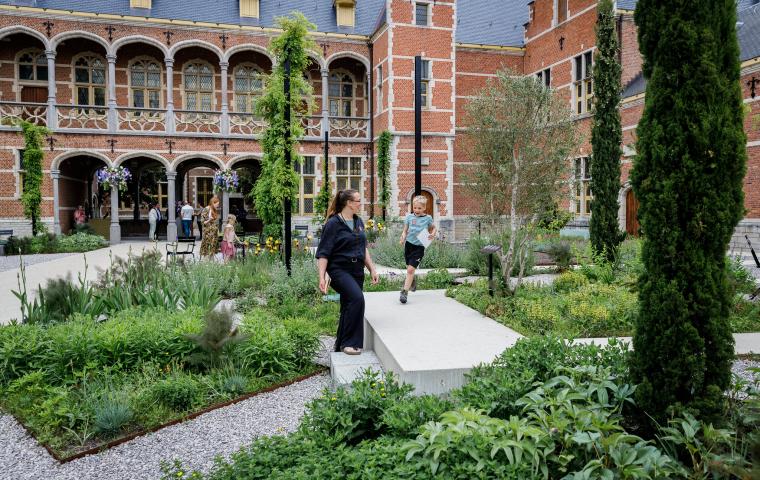 Een kind rent al lachend in een weelderige tuin, een volwassene kijkt toe.