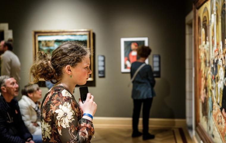 Een kind houdt een audiogids vast en kijkt naar een schilderij.