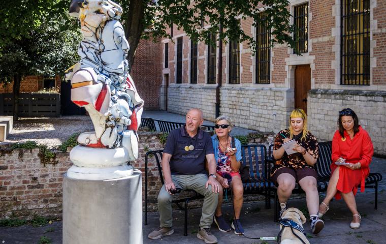 Menschen sitzen draußen auf einer Bank neben einem modernen Kunstwerk