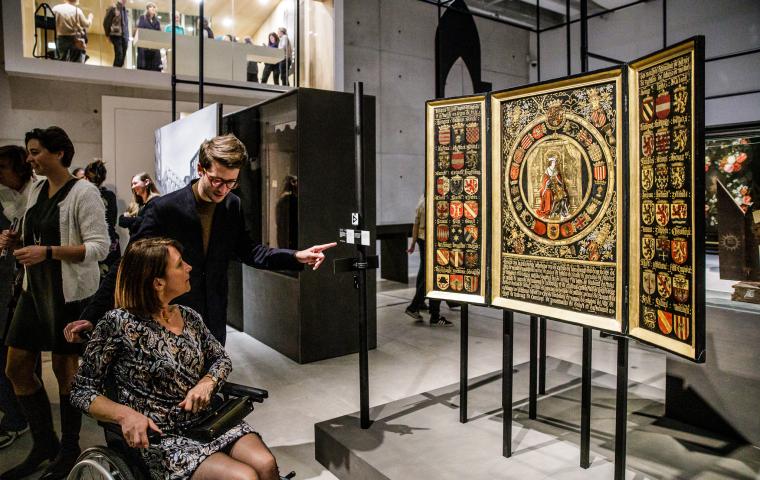 Twee bezoekers kijken naar een drieluik in een drukke museumzaal.