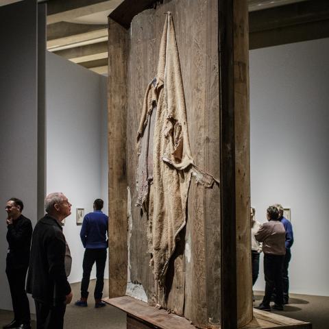 Een groot hedendaags kunstwerk gemaakt uit textiel en een houten kader staat centraal in een zaal.