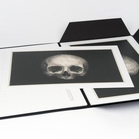 A black book, filled with prints of drawings, lies open.