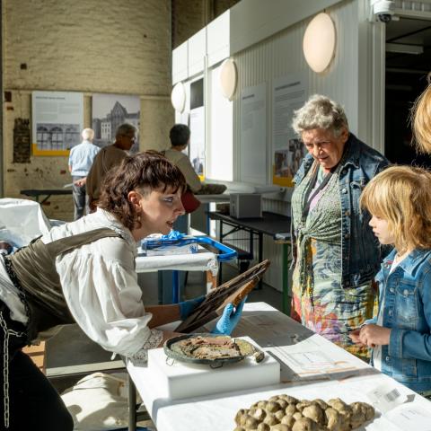 Iemand met blauwe handschoenen geeft uitleg bij objecten aan twee kinderen.