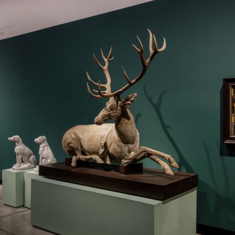 Een grote sculptuur van een hert staat in een groene museumzaal.
