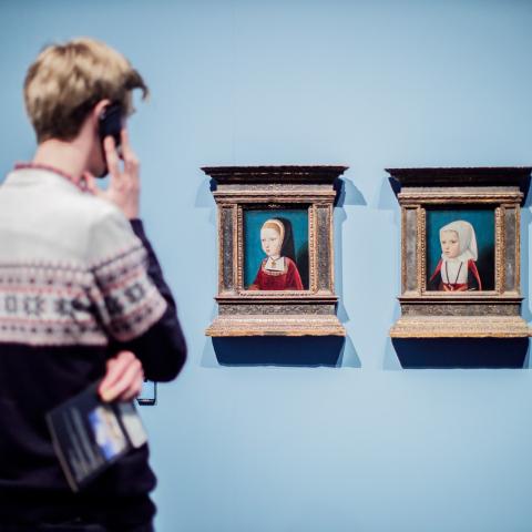 Een bezoeker met audiogids kijkt naar twee kleine portretten.