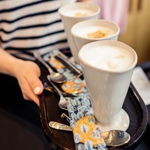 Close-up van iemand die een plateau met 3 kopjes koffie draagt.