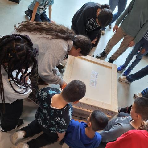 Een groep kinderen zit rond een gesloten houten kist.