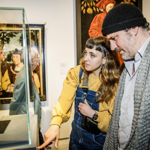 Twee mensen kijken naar een ovalen schilderij in een vitrine.