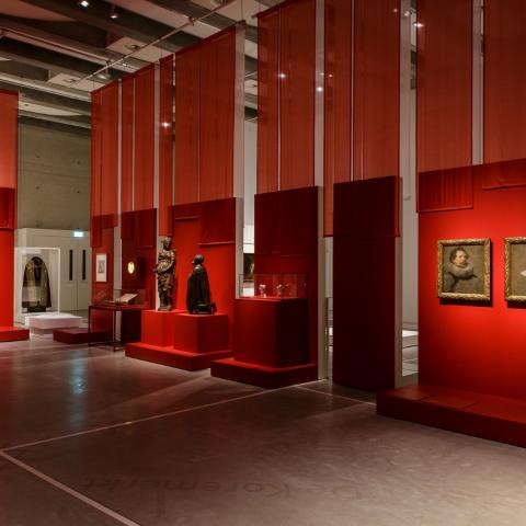 Een grote museumzaal met rode wanden en doeken.