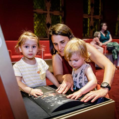 Een volwassen persoon met twee kinderen kijken naar en voelen aan een speelelement.