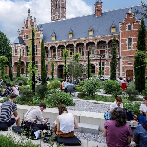 Bezoekers zitten in een tuin opgedeeld in perkjes, op de achtergrond is de gevel van het stadspaleis te zien.