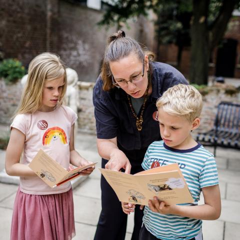 Twee kinderen kijken boekjes, een volwassen persoon helpt hen.