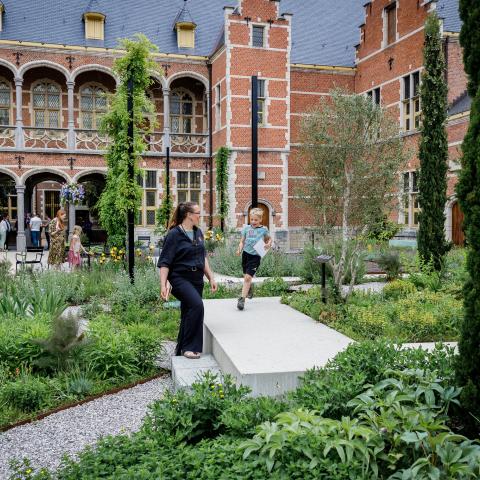 Een kind rent al lachend in een weelderige tuin, een volwassene kijkt toe.