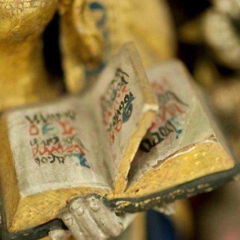 Detail van verguld beeldje: een hand die een open boek vasthoudt.