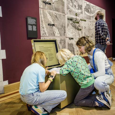 Twee kinderen en een volwassene zitten rond een goudkleurig open kastje.