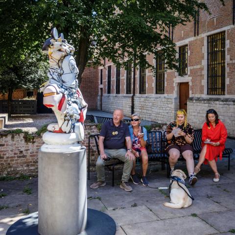 Mensen zitten buiten op een bank naast een modern kunstwerk
