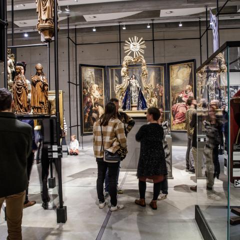Een drukke museumzaal met vele werken, zoals een Madonna beeldje.